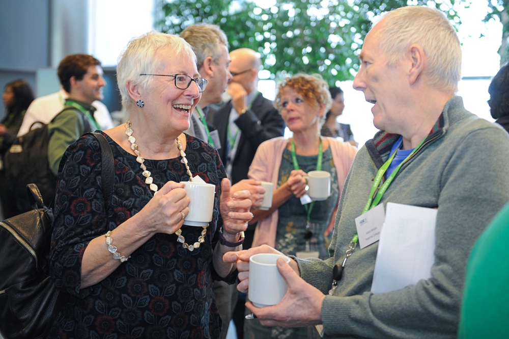 Attendees at a community engagement event chatting and smiling while holding mugs.